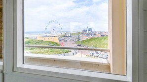 A view from a window overlooking a coastal town with a prominent Ferris wheel, a parking lot, and buildings in the distance. - Apartment Near North Sea and Lighthouse (Egmond aan Zee)