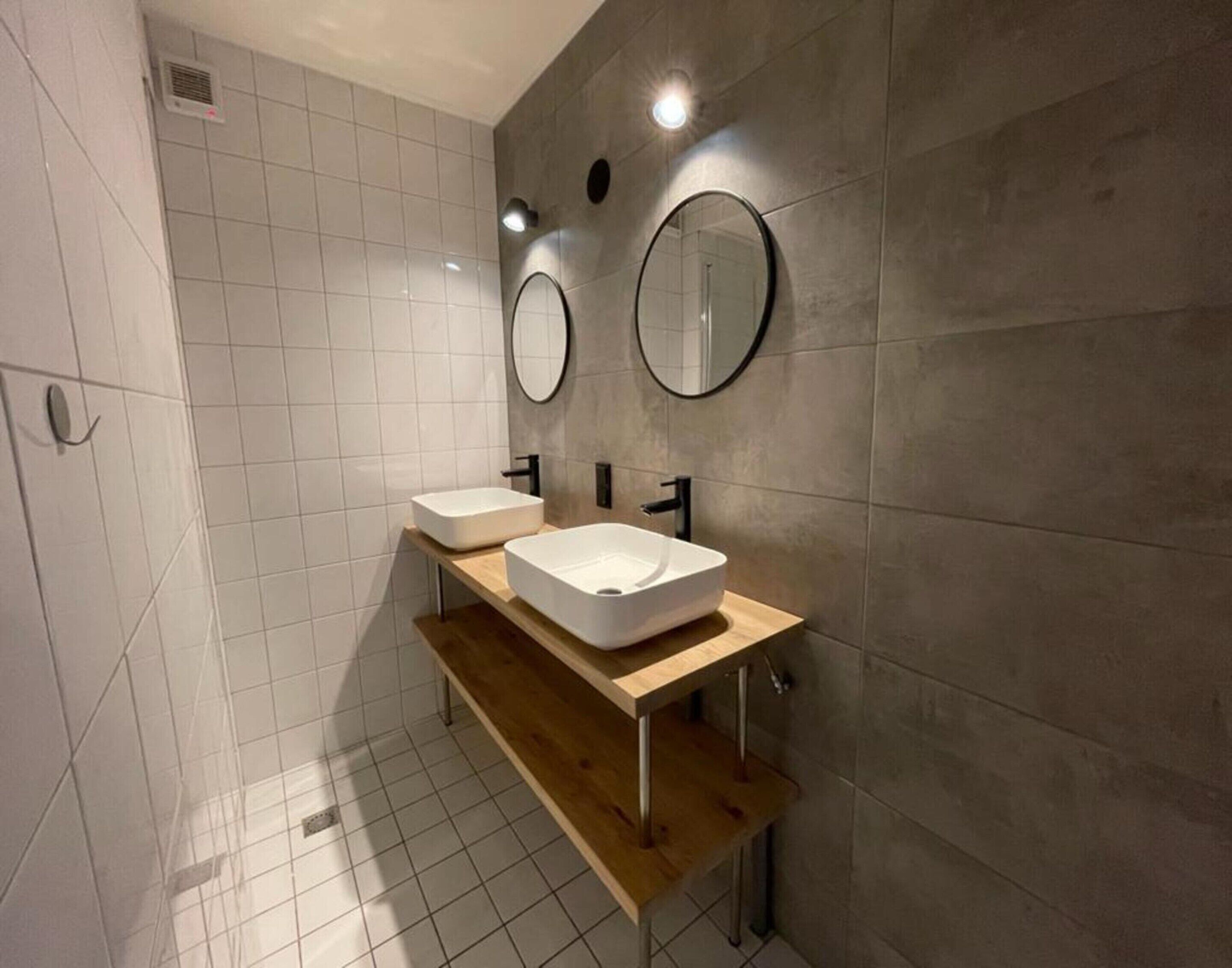 A modern bathroom with two white sinks, a wooden vanity, and two wall-mounted mirrors.