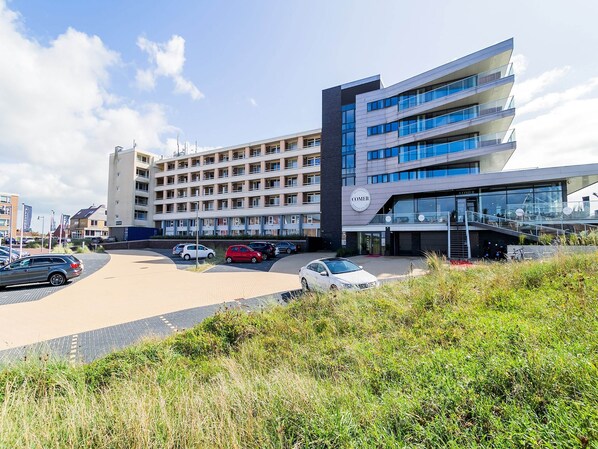 A modern hotel with multiple floors, a parking lot, and a landscaped area with grass.