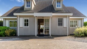 A two-story house with a tiled roof, a front entrance with a glass door, and a driveway leading to the entrance.