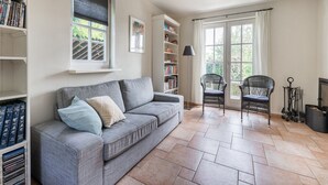 A living room with a grey sofa, a bookshelf, two wicker chairs, a floor lamp, and a fireplace.
