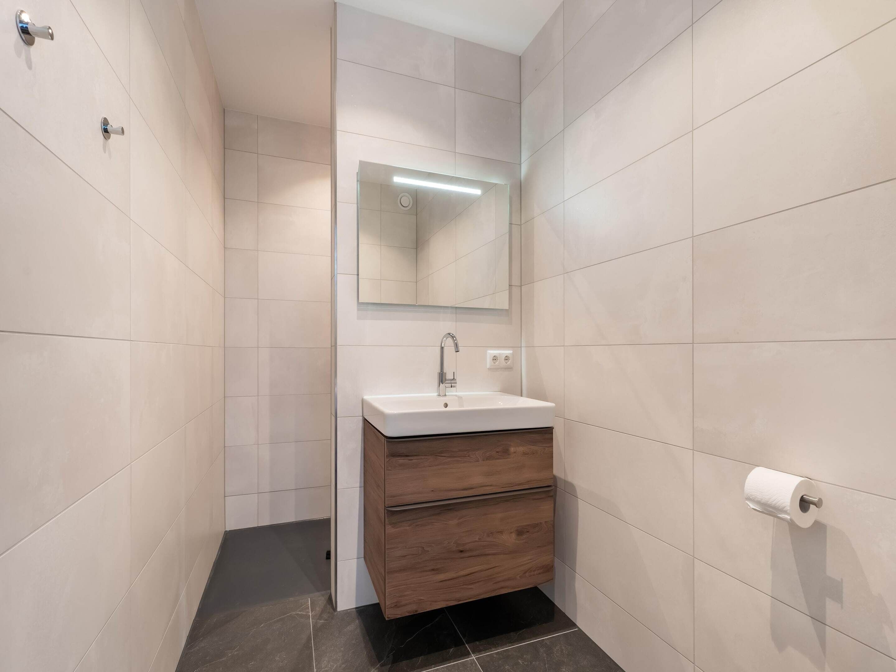 A modern bathroom with a white sink, wooden vanity, and a mirror above it.