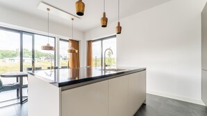 A modern kitchen with a large island, pendant lights, and large windows offering a view of the outdoors. - Villa in Zeewolde Near Flevostrand Beach (Zeewolde)
