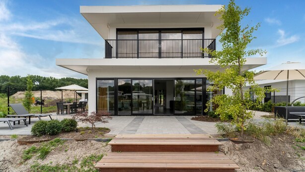 A modern two-story building with a balcony, outdoor seating, and a paved entrance area. - Villa in Zeewolde Near Flevostrand Beach (Zeewolde)