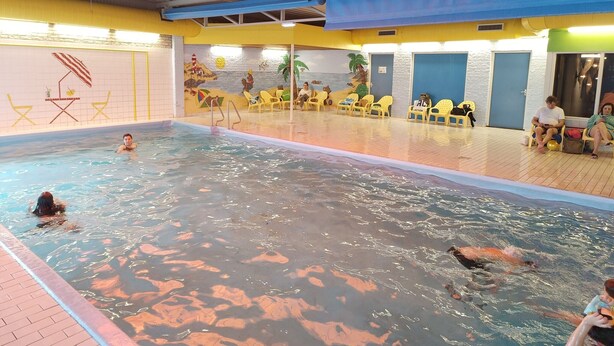 Une piscine intérieure dotée de plusieurs couloirs, de murs jaunes et bleus, et d’une fresque représentant une scène de plage.