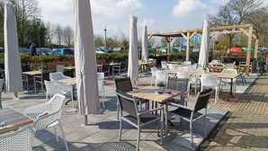 Un café en plein air avec des tables et des chaises, protégé par des auvents blancs, et une pergola en bois en arrière-plan.