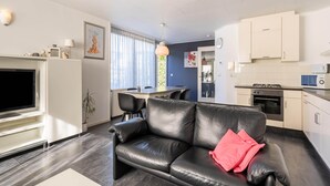 Un salon moderne avec un canapé en cuir noir, un téléviseur à écran plat et un coin repas comprenant une table et des chaises.