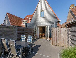 A patio area with a table and chairs, a wooden fence, and a building with a sloped roof. - Holiday Home in Domburg Near the Beach (Domburg)