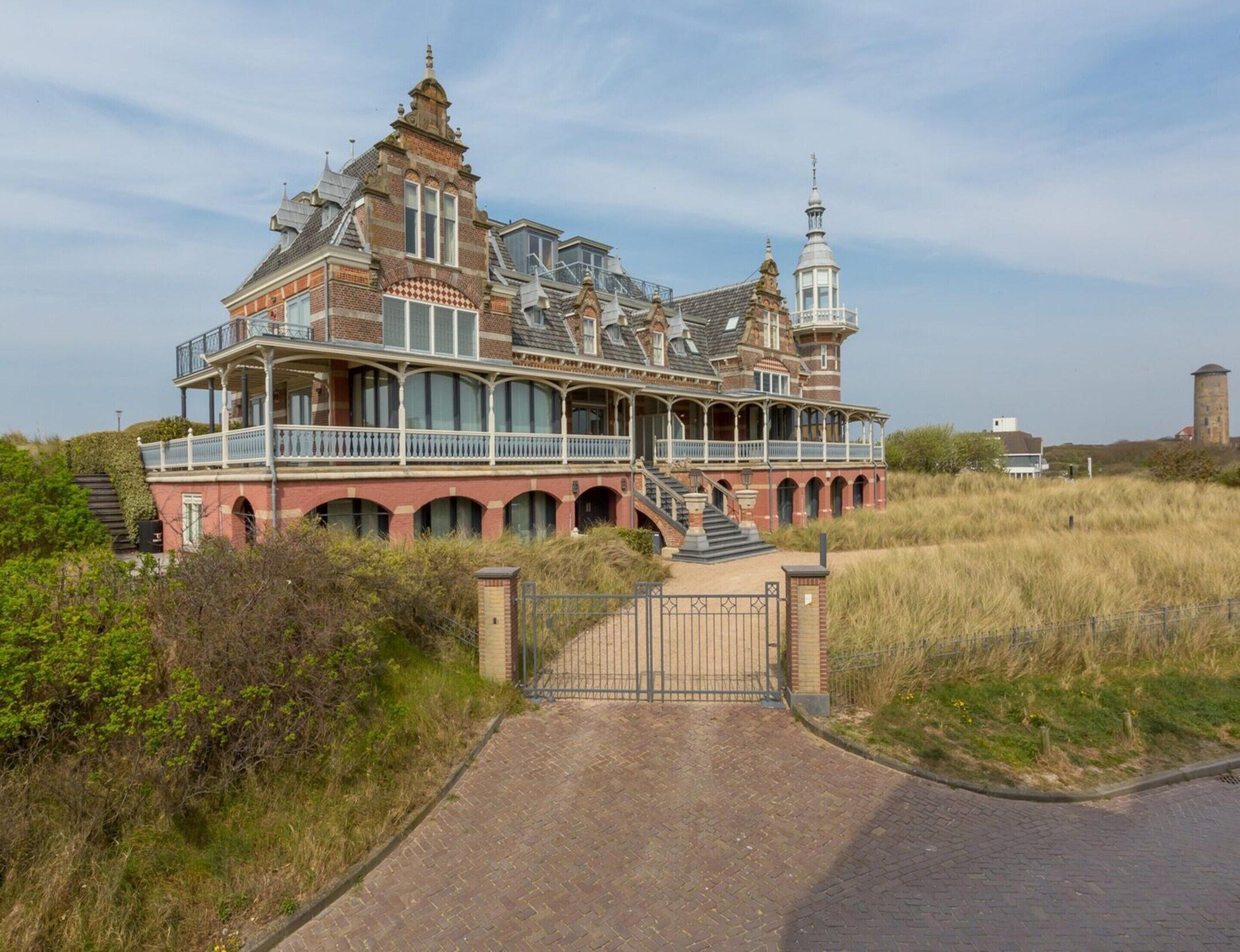 A large, historic house with multiple balconies, a tower, and a prominent entrance gate.