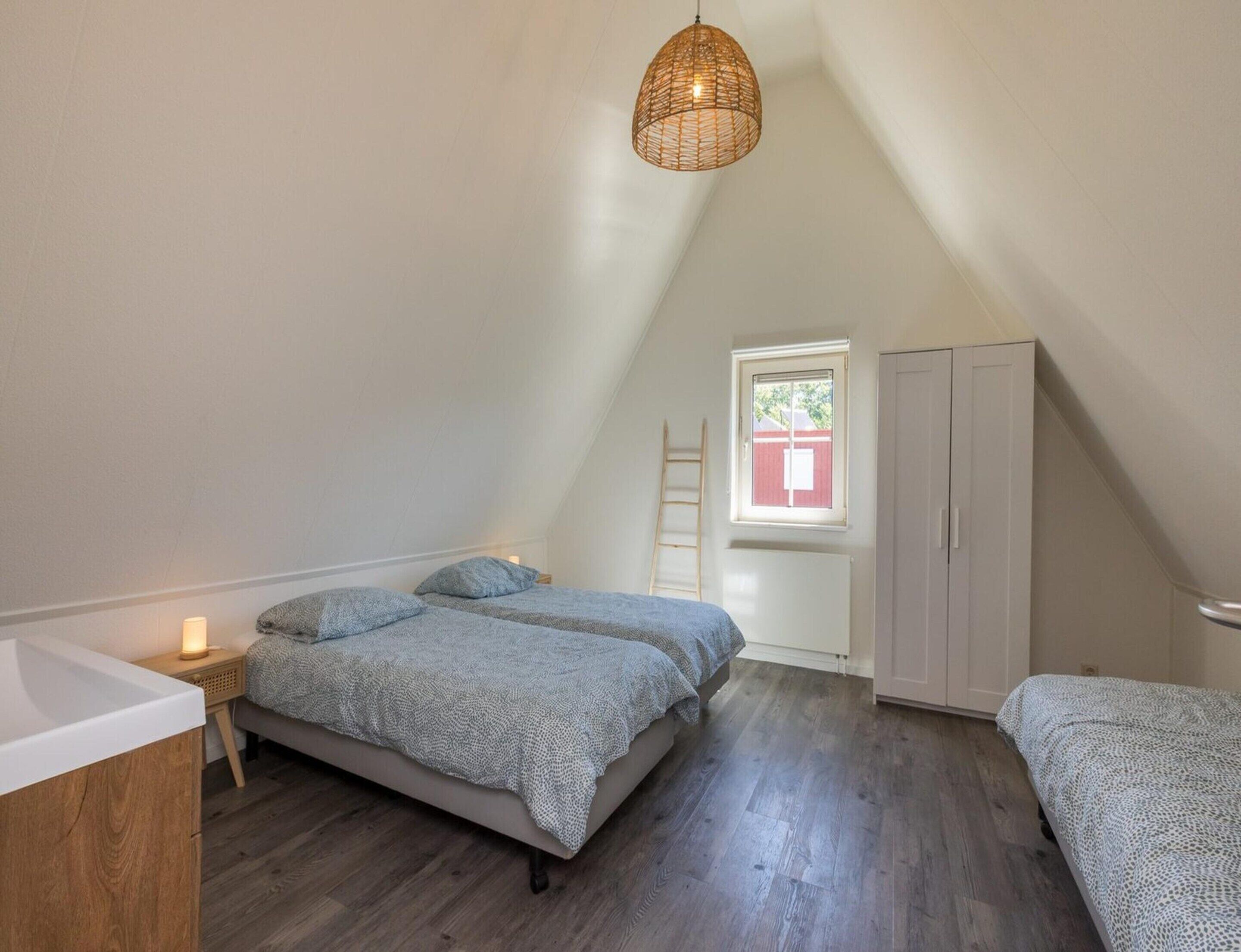 A bedroom with a sloped ceiling, a bed with a patterned blanket, a bedside table with a lamp, and a wardrobe.