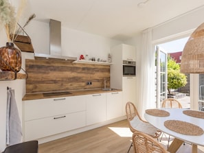 Une cuisine moderne avec des meubles blancs, un pare-feu en bois et un coin repas comprenant des chaises en osier et une table ronde.