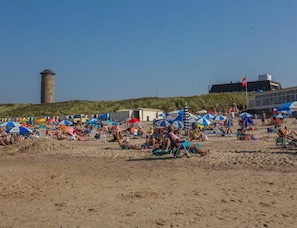 A beach with people sunbathing, umbrellas, and a lighthouse in the background. - Holiday Home in Domburg Near the Beach (Domburg)