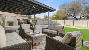 Une terrasse couverte, meublée de mobilier en osier, avec un barbecue et une piscine.