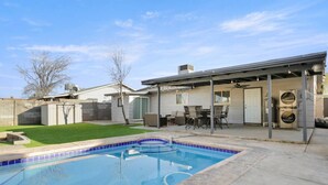 Un jardin à l’arrière d’une maison, comprenant une piscine, des meubles de patio et un espace de détente extérieur abrité.