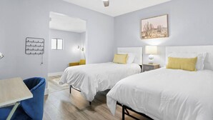 Une chambre d’hôtel avec deux lits, un bureau, une chaise, un ventilateur de plafond et un luminaire fixé au mur.