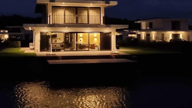Una casa moderna de dos pisos con un amplio acceso de vidrio y una piscina delantera.