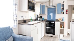 A compact kitchen with a stove, oven, and a microwave. There is a dining area with a blue sofa and a small table. - Chalet in Renesse Near Sandy Beaches (Renesse)