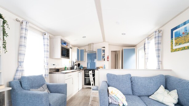 A modern kitchen with white cabinets, a black stove, and a blue sofa in the living area. - Chalet in Renesse Near Sandy Beaches (Renesse)