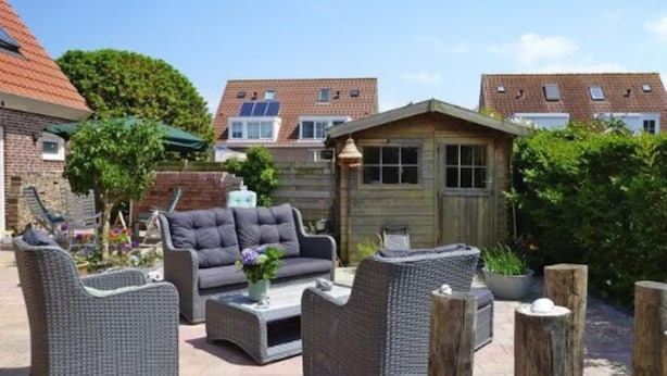 Un espace extérieur aménagé en terrasse, avec des meubles en osier, notamment un canapé et des fauteuils, ainsi qu’une petite structure en bois.