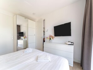 A modern hotel room with a large bed, a flat-screen TV mounted on the wall, a dresser, and a mirror.