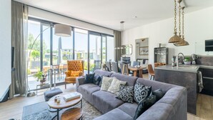 A modern living room with a grey sofa, a round wooden table, and a large window offering a view of the outdoors.