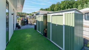 A modern building with a covered patio area, green artificial grass, and metal storage sheds.