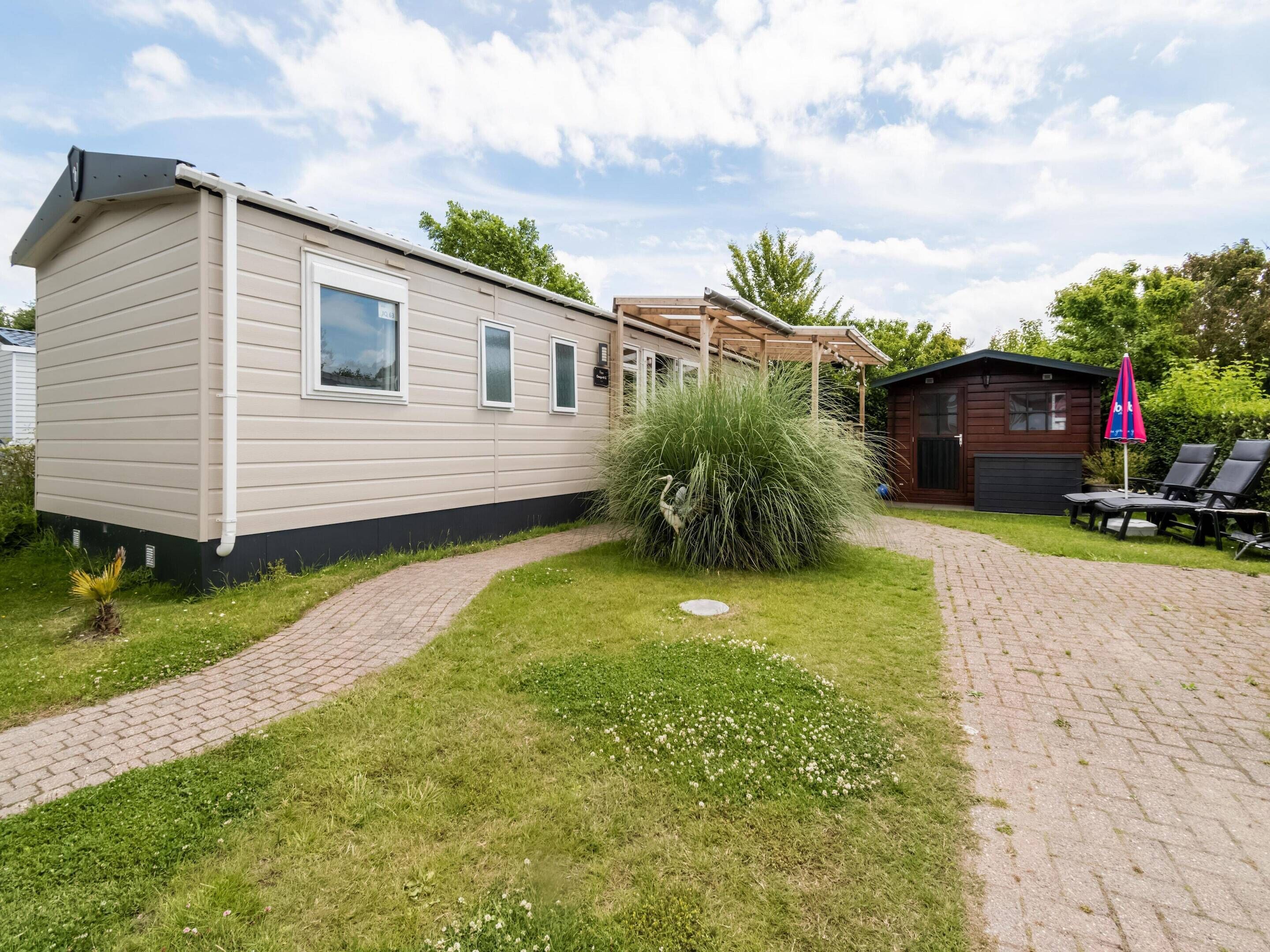 A mobile home with a paved driveway, a small garden, and a wooden structure with a covered patio.