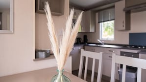 Ein Esstisch mit einer Vase mit Pampasgras, weißen Stühlen und einer Küche im Hintergrund.