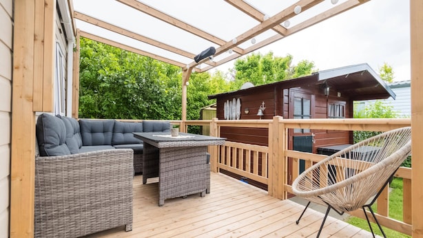 Eine Holzterrasse mit einer Couch und einem Sessel, einem kleinen Tisch und einem Hollerleger.