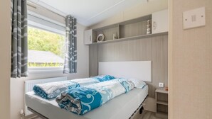 Ein modernes Schlafzimmer mit Bett, einem Fenster mit Vorhängen, einem Nachttisch und einem Regal mit Dekoration.