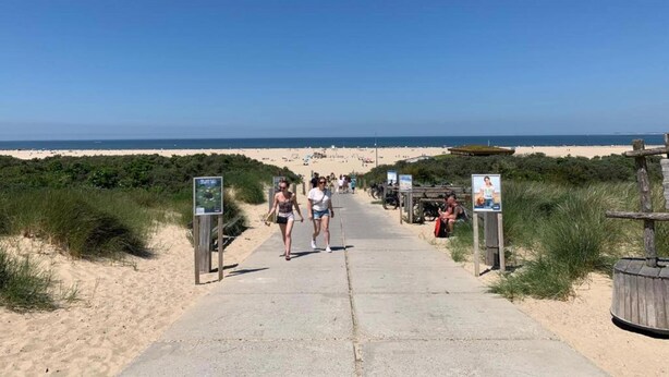 Een betonnen pad dat naar een zandstrand leidt, met informatietekens aan weerszijden.