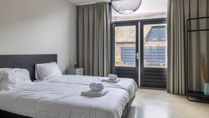 Een moderne slaapkamer met een groot bed, twee nachtkastjes en een schuifdeur naar een balkon.