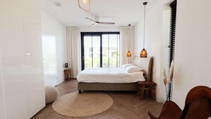 A modern bedroom with a large bed, a ceiling fan, and a view of greenery outside. - Villa in Zeewolde With Private Terrace (Zeewolde)