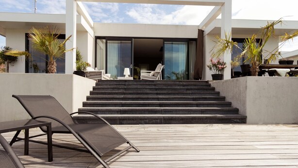 A modern outdoor area with a wooden deck, a lounge chair, and a set of stairs leading to a building with large glass doors. - Villa in Zeewolde With Private Terrace (Zeewolde)