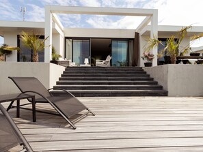 A modern outdoor area with a wooden deck, a lounge chair, and a set of stairs leading to a building with large glass doors. - Villa in Zeewolde With Private Terrace (Zeewolde)