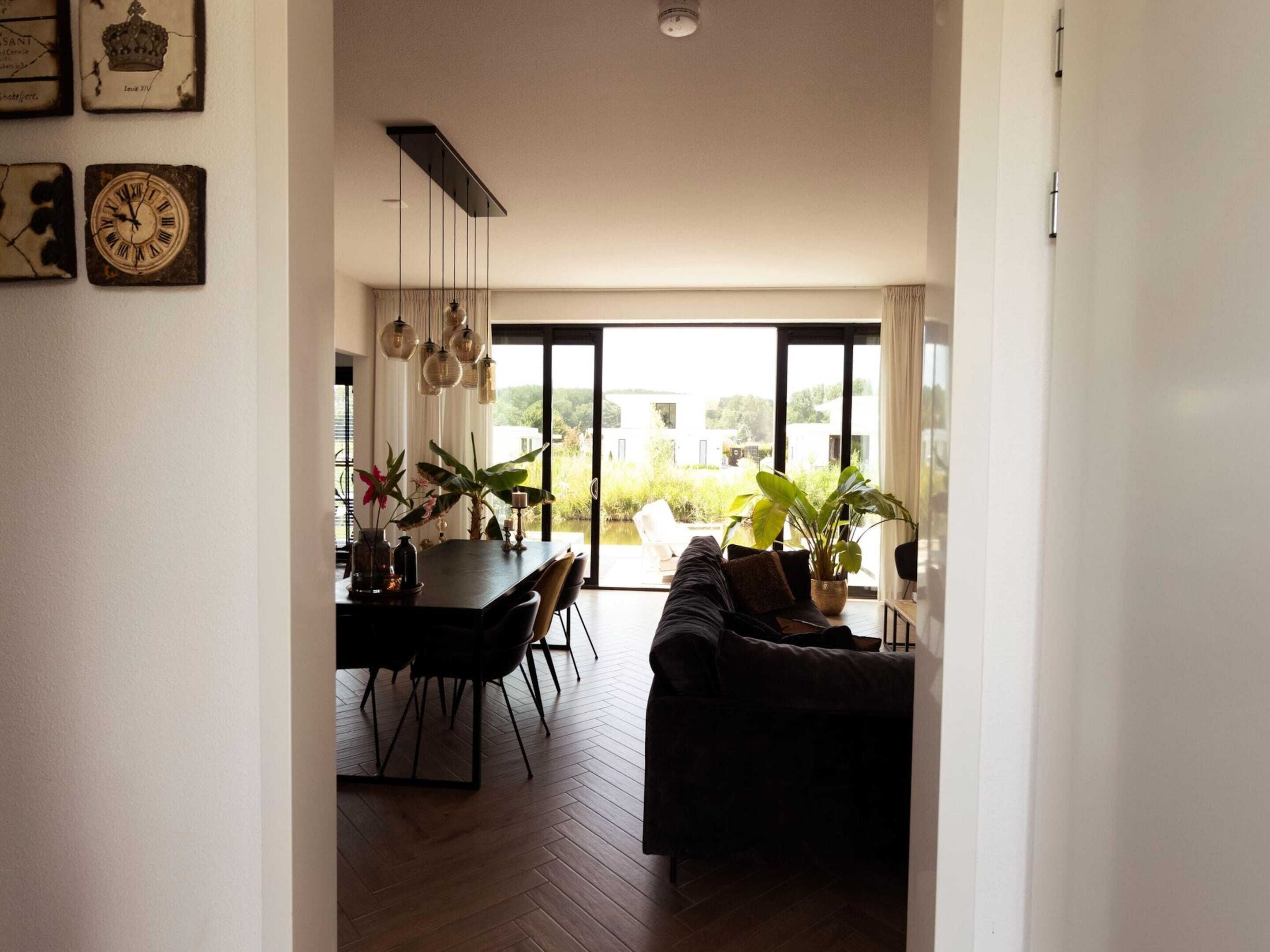 A modern living room with a dark sofa, a dining table with chairs, and a large window offering a view of greenery outside.