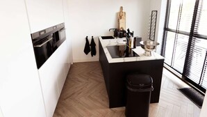 A modern kitchen with white cabinets, a black countertop, and a wooden herringbone floor. - Villa in Zeewolde With Private Terrace (Zeewolde)