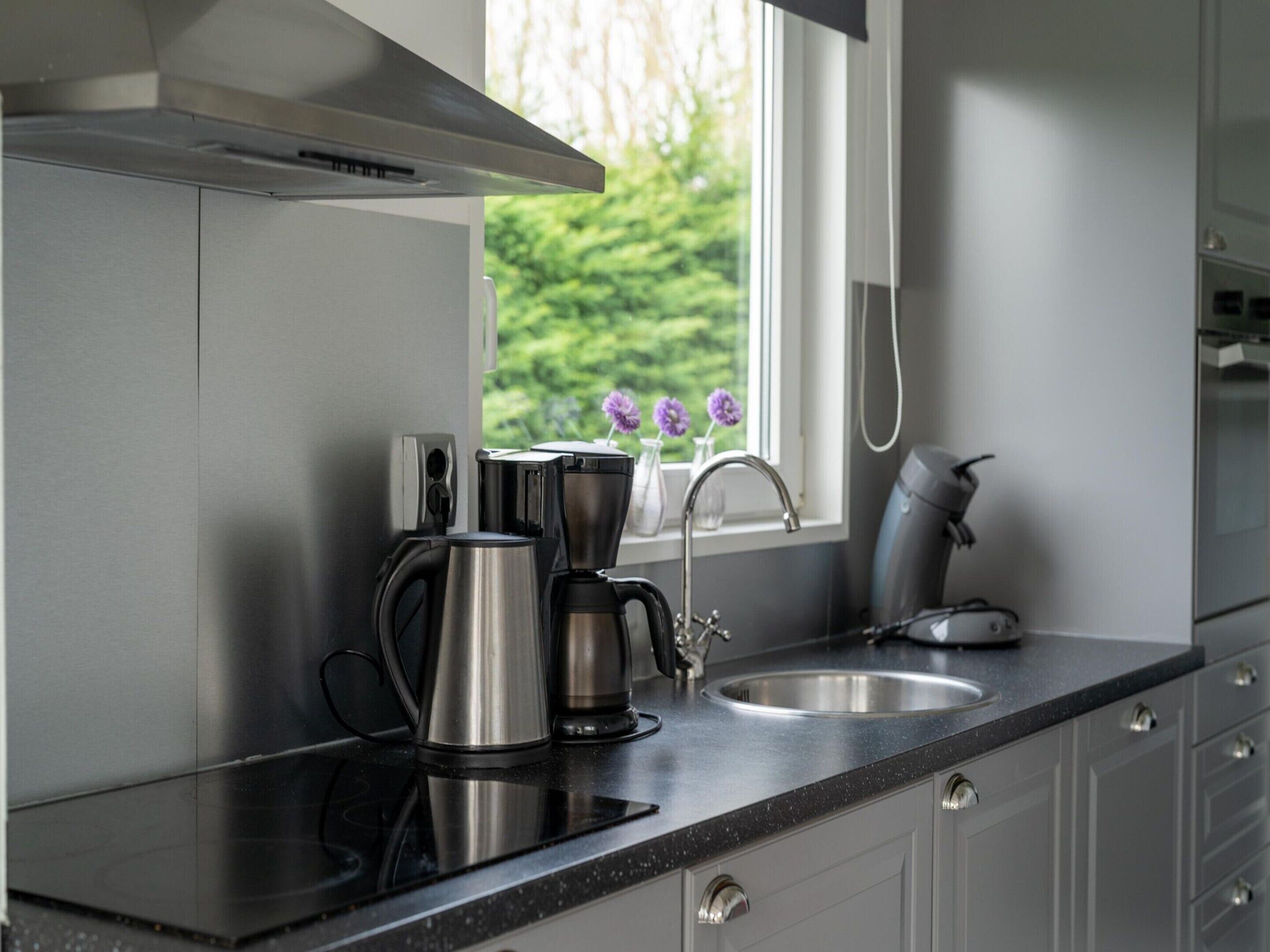 Een moderne keuken met roestvrijstalen apparatuur, een raam met uitzicht op groen en een zwart aanrecht.