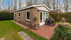Une maison de plain-pied avec une façade en briques, de grandes fenêtres et un patio aménagé avec une table et des chaises.