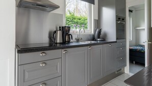 Une cuisine moderne avec des meubles gris, une hotte en acier inoxydable, une machine à café et une fenêtre donnant sur un paysage verdoyant.