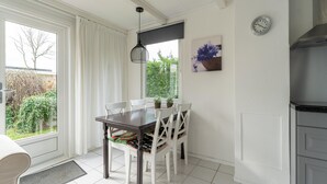 Un espace repas comprenant une table et des chaises, un luminaire suspendu, une horloge et une vue sur la verdure à l’extérieur.