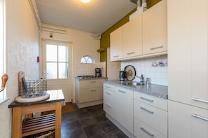 A kitchen with white cabinets, a window, and a countertop with a coffee maker. - Home Zoutelande Near Beach (Zoutelande)