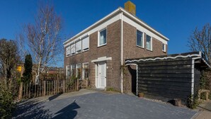 A two-story brick house with a white door, a small attached shed, and a paved driveway. - Home Zoutelande Near Beach (Zoutelande)