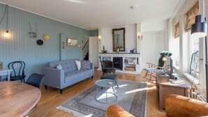 A living room with a sofa, a dining table, a fireplace, and a staircase. - Home Zoutelande Near Beach (Zoutelande)