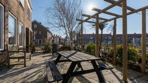 A wooden pergola with a picnic table, benches, and a brick building in the background. - Home Zoutelande Near Beach (Zoutelande)