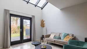 A modern living room with a sofa, two round tables, and a large sliding glass door leading to a garden.