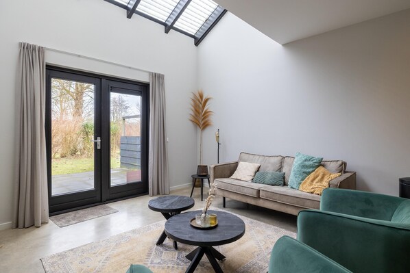 A modern living room with a sofa, two round tables, and a large sliding glass door leading to a garden.