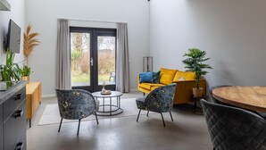 A modern living room with a sofa, two armchairs, a round wooden table, and a TV on a cabinet.