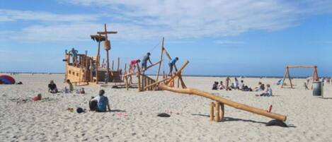 A beach with wooden play structures and a long wooden beam.