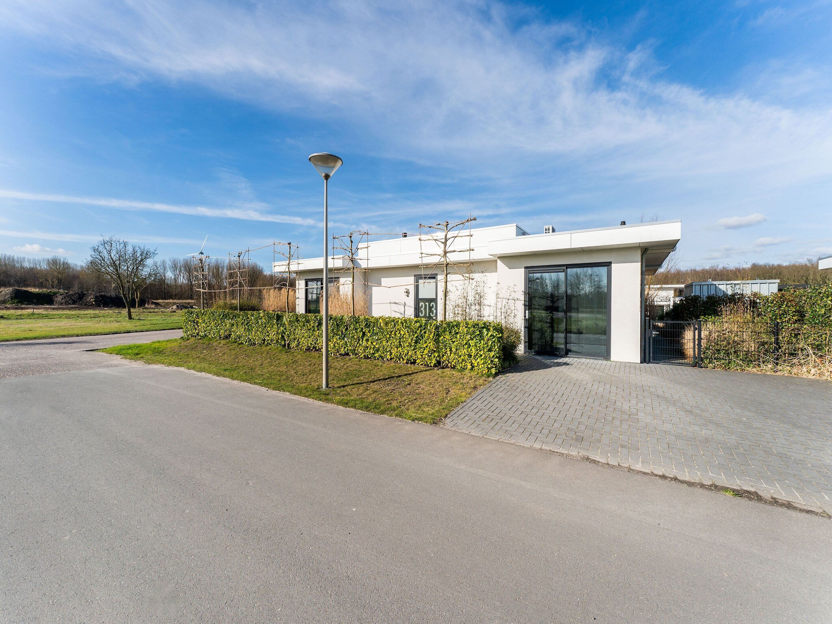 A modern building with a paved driveway, a metal lamp post, and a hedge.